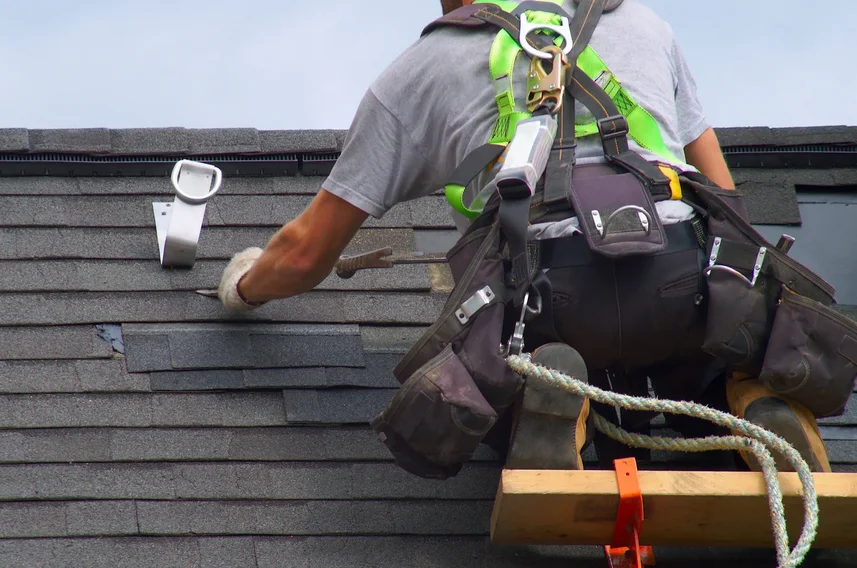 Roofer in a safety harness working near a roof pipe vent