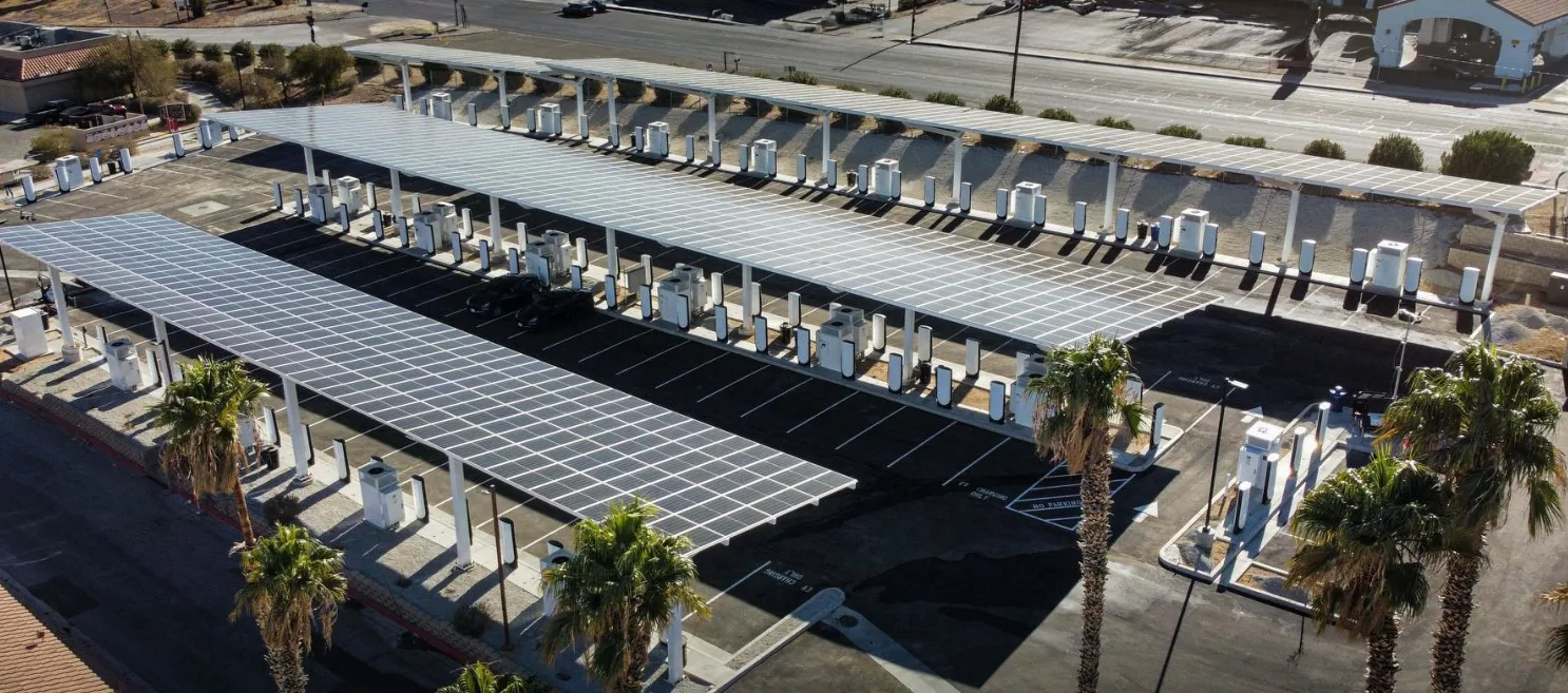 Aerial view of a large Tesla Supercharger site under solar canopies