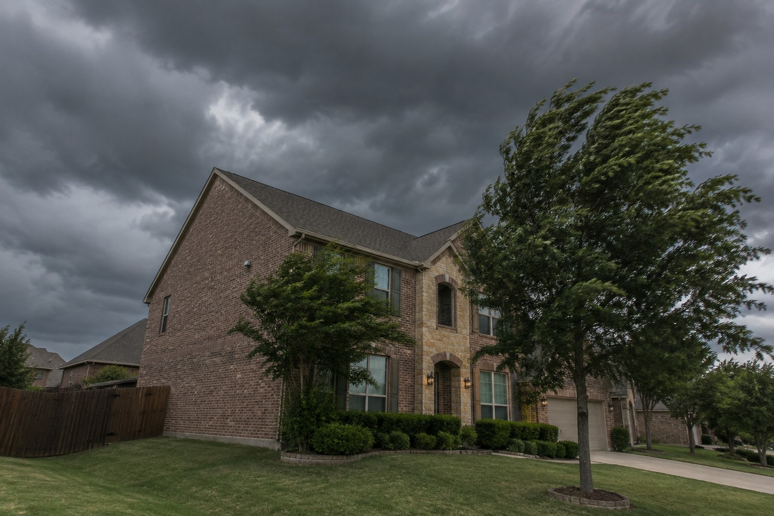 Brick home with a tall gable end wall under dark North Texas storm clouds