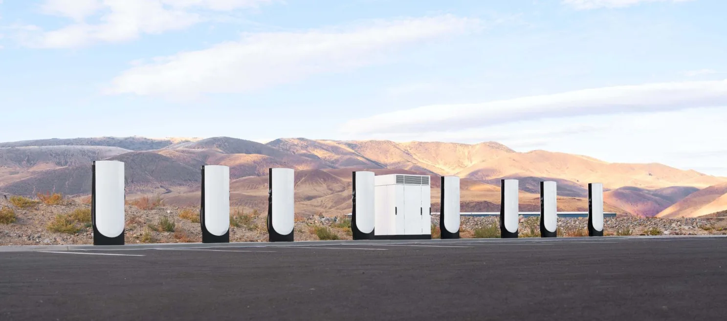 Row of Tesla V4 Supercharger posts and a power cabinet at a commercial charging site