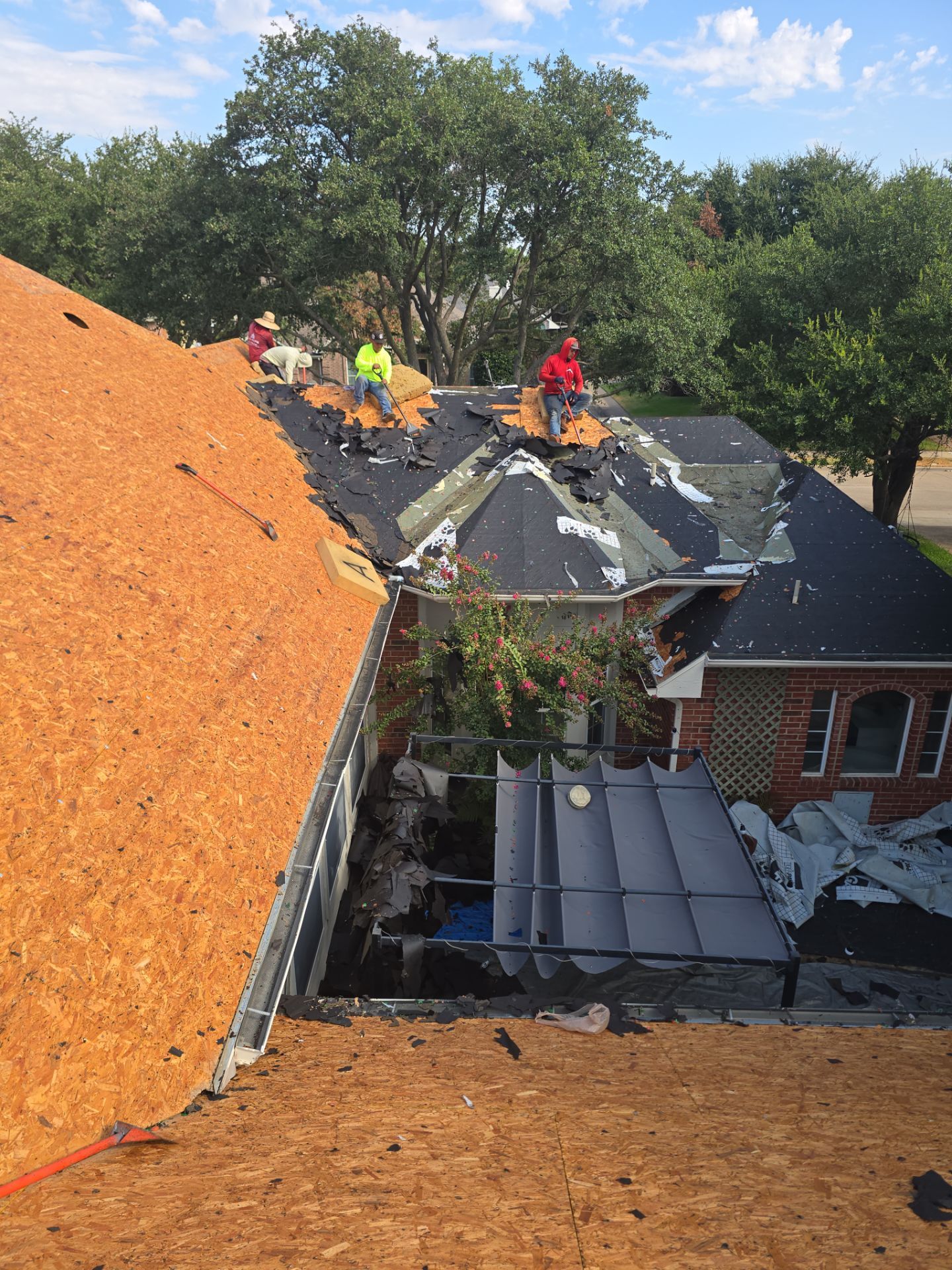 Roofing crew tearing off shingles on a two-story home