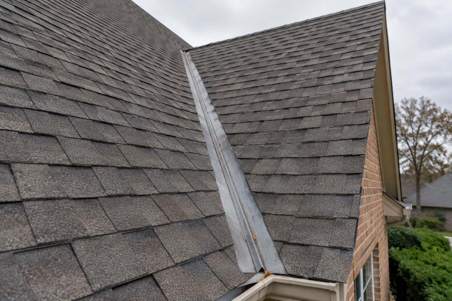Open roof valley with exposed metal channel running between two sections of gray asphalt shingles