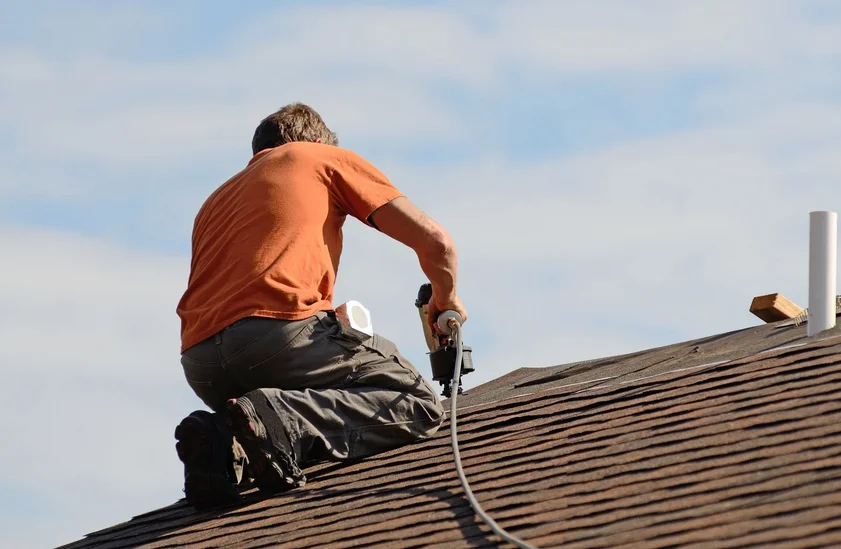 Roofer nailing shingles near a plumbing vent pipe