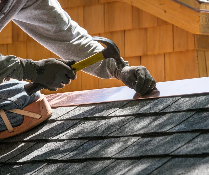 Roofer hammering metal flashing over shingles